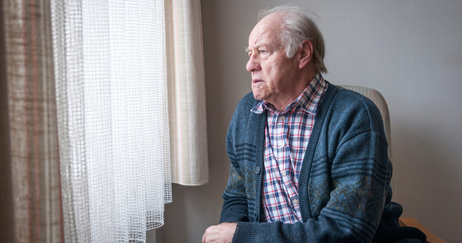 Older man sitting alone beside a window