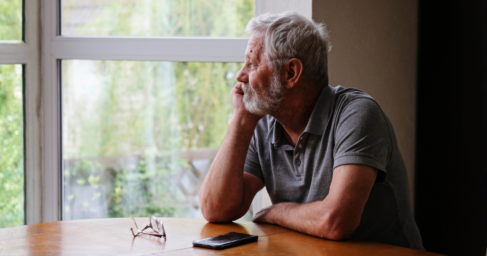 Older grey-haired man sitting at a table by a window