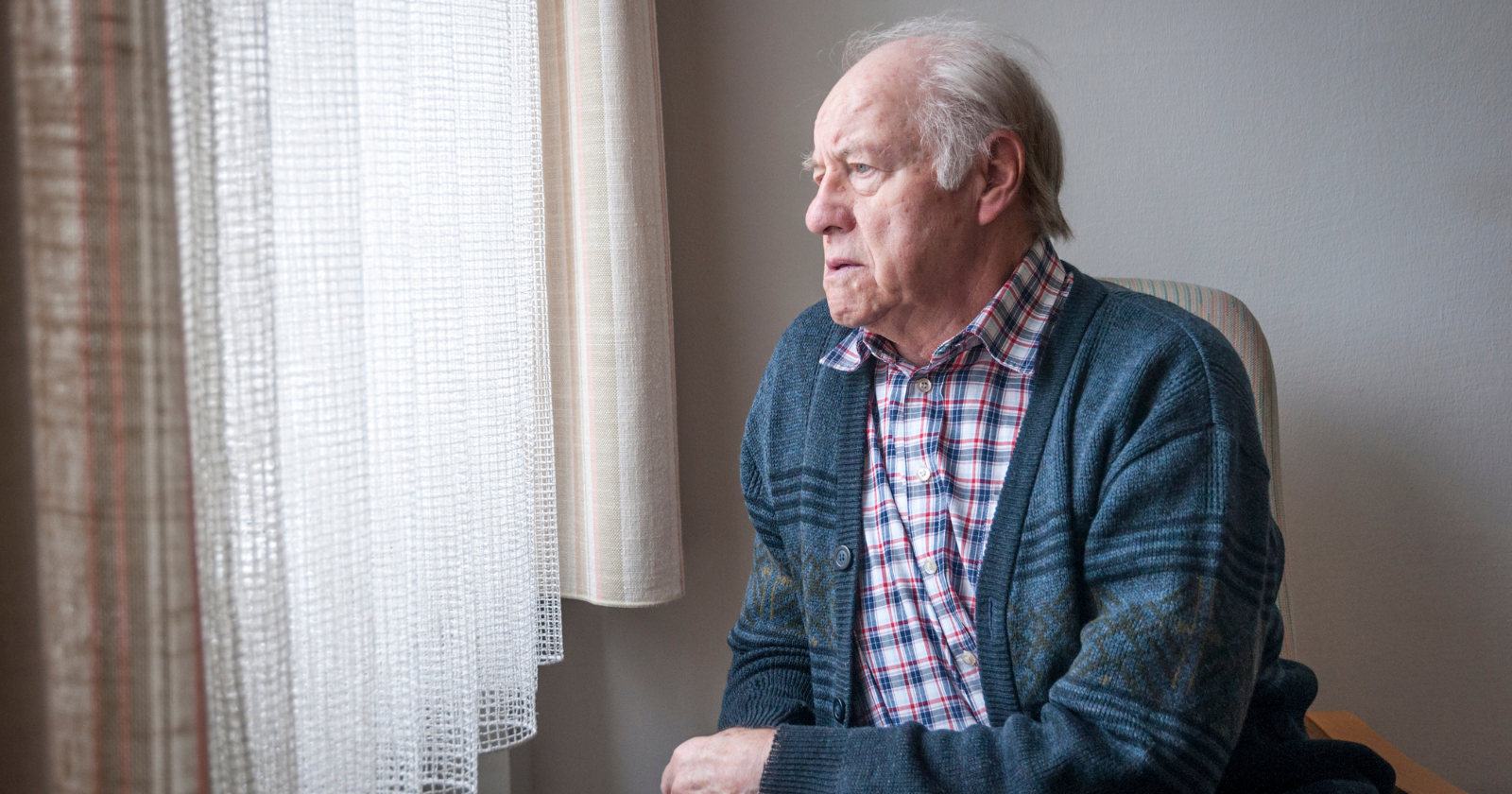 An older man sitting beside a window and looking outside