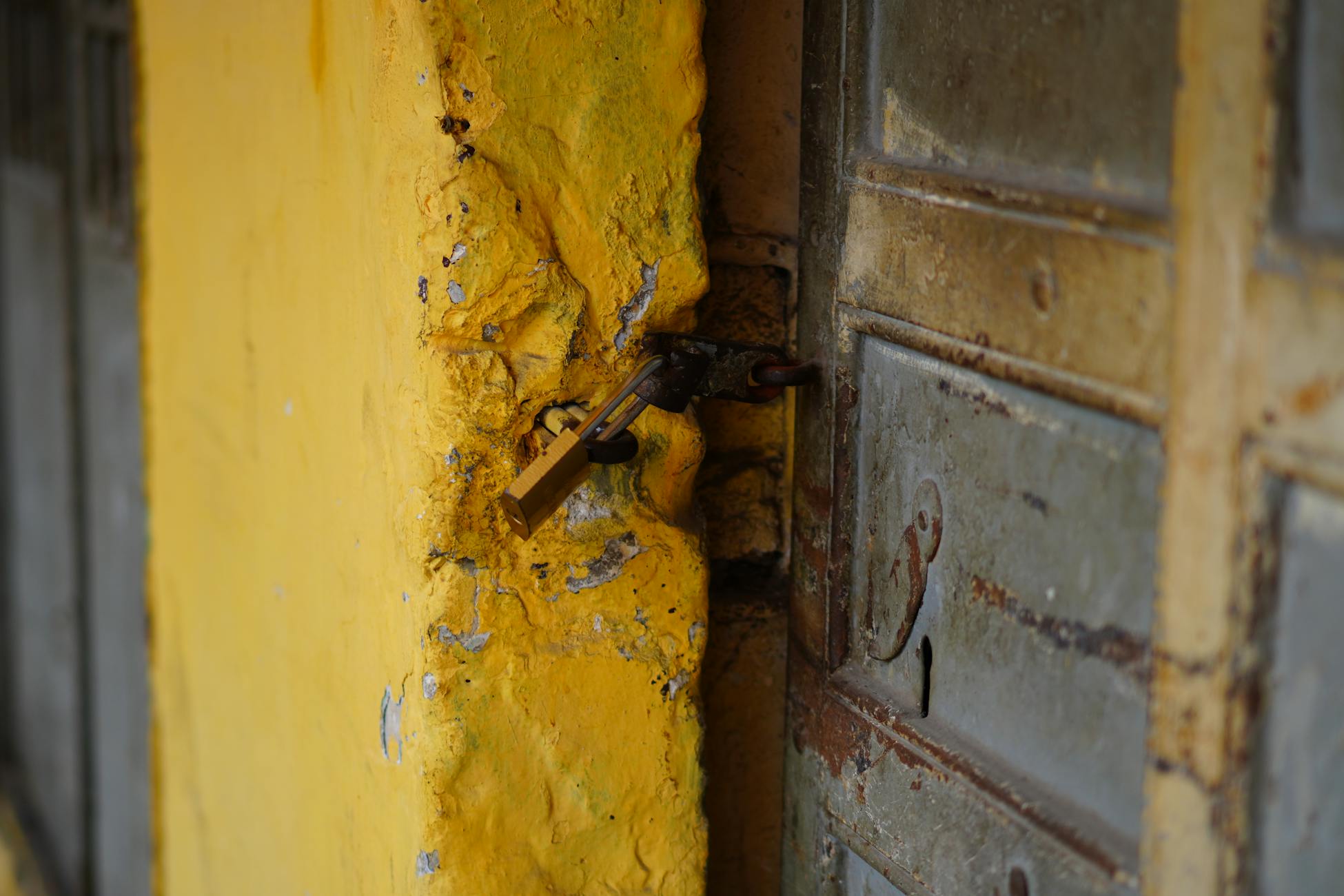 Close-up of a locked weathered metal door and textured yellow wall, symbolizing security.