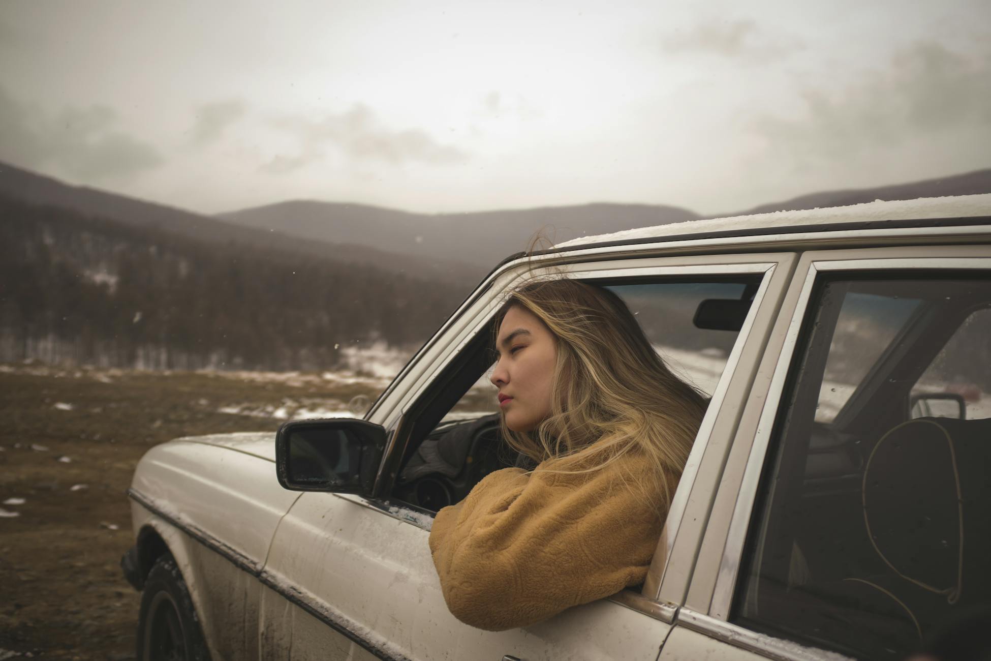 A woman in a car enjoying the snowy mountain view during a winter drive.