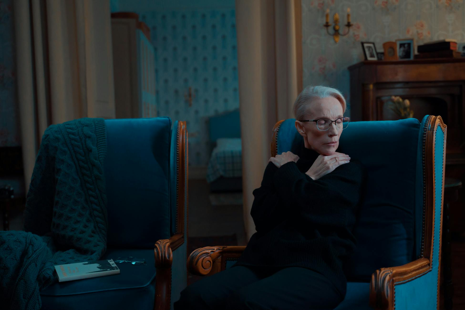 Senior woman sitting thoughtfully in a vintage armchair indoors, exuding a serene and contemplative mood.
