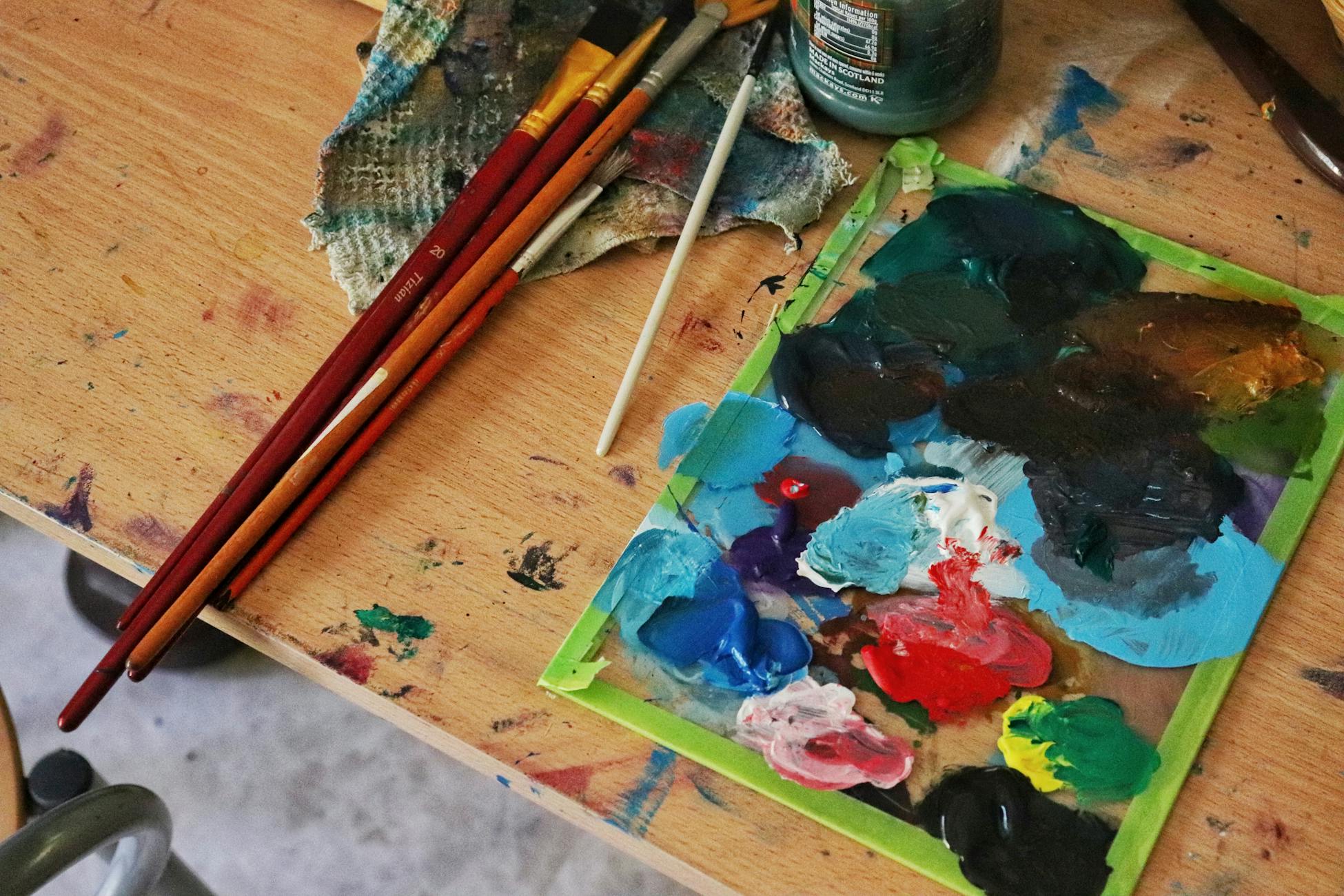 Colorful paint palette and brushes on a wooden table showcasing an artist's creative workspace.