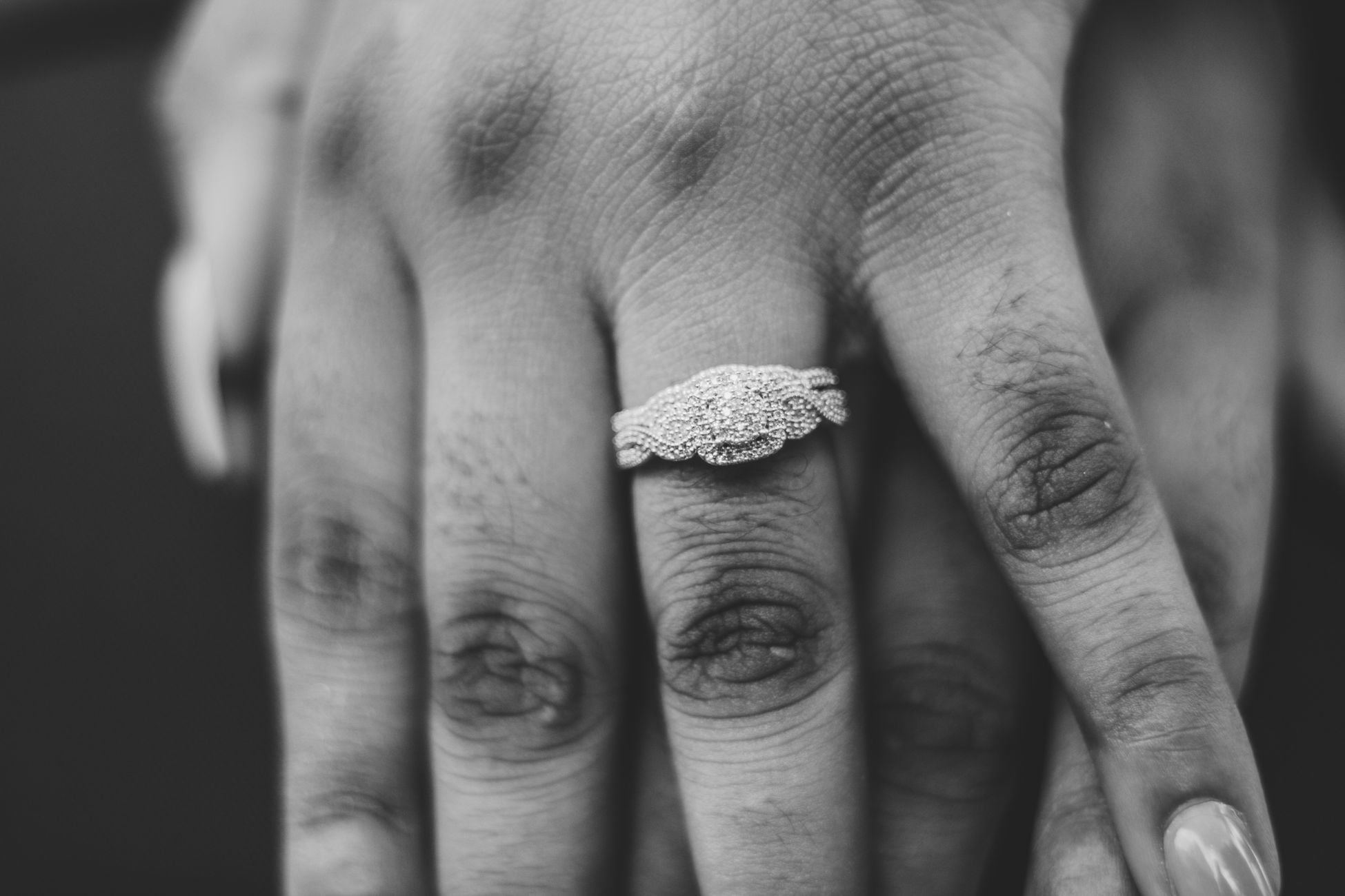 A close-up black and white image showcasing a woman's diamond engagement ring on her hand.