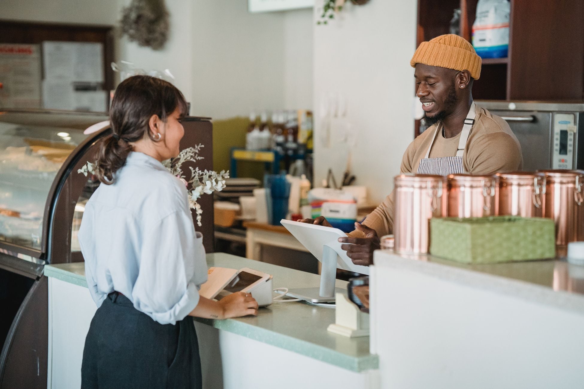 A barista and customer enjoy a friendly interaction at a café counter with a warm ambiance.