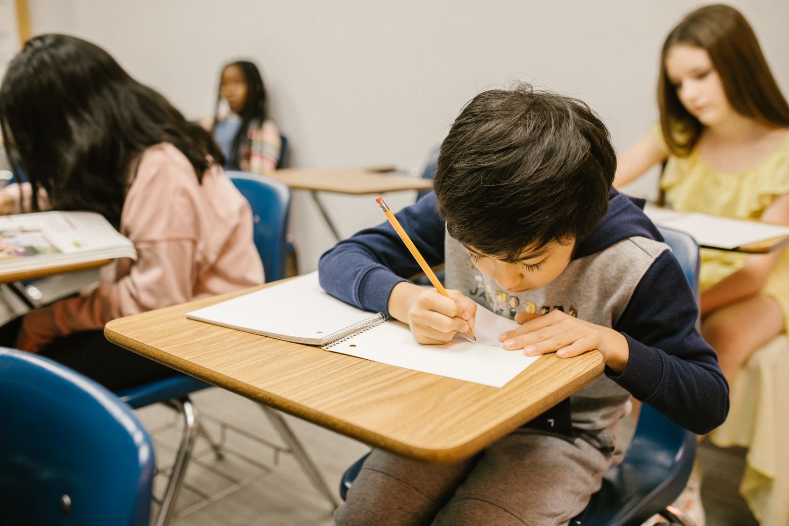 A school-age boy writing in a notebook while other children work at classroom desks