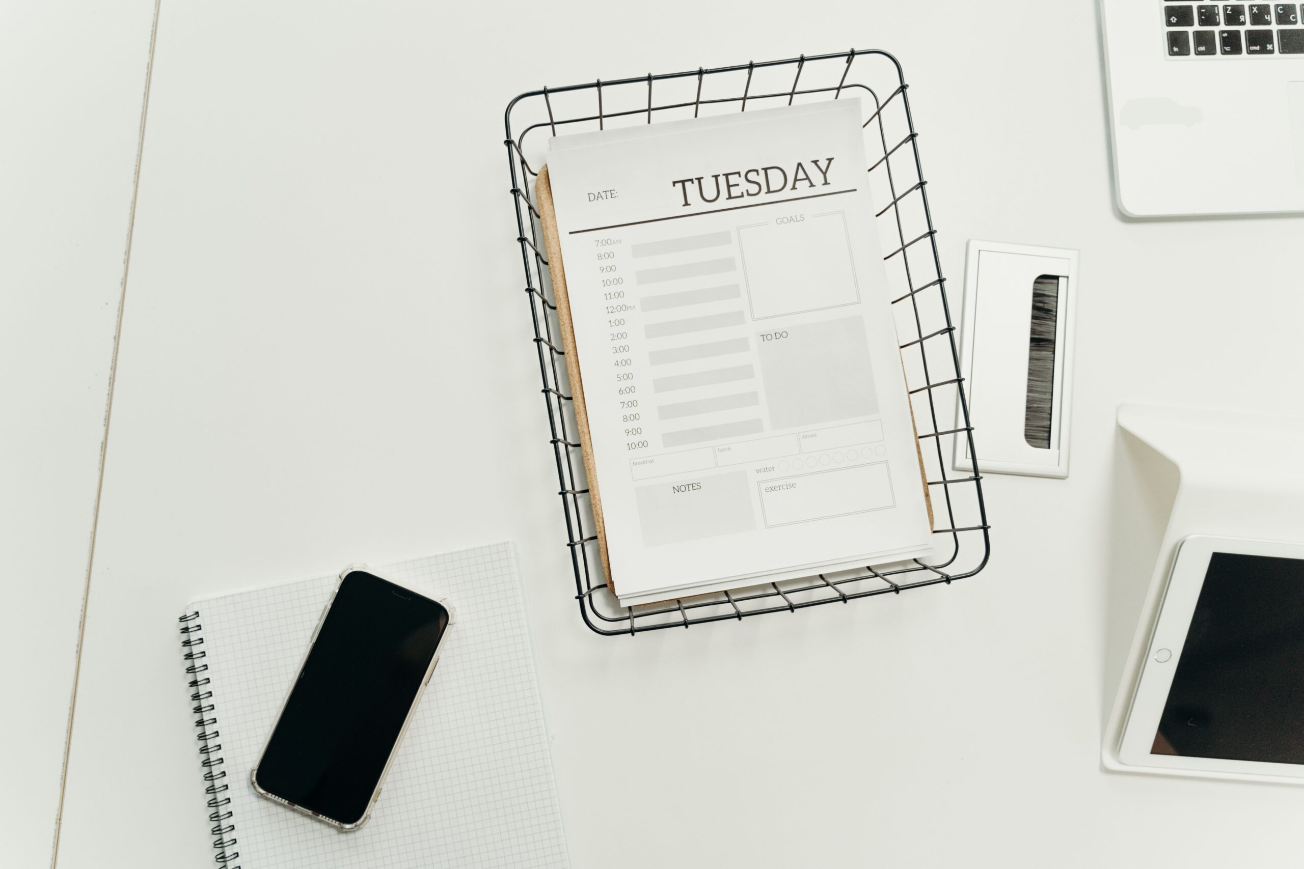 Top view of a paper day planner and smartphone on a white office desk
