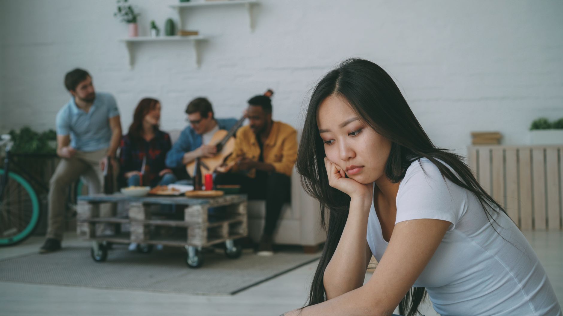 A thoughtful woman sitting apart while friends socialise behind her