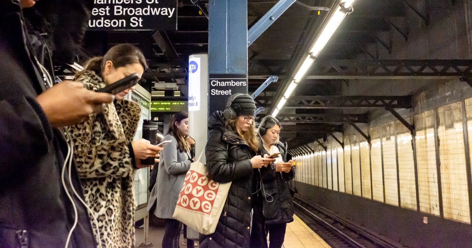 Commuters on a New York subway platform, all looking down at their phones