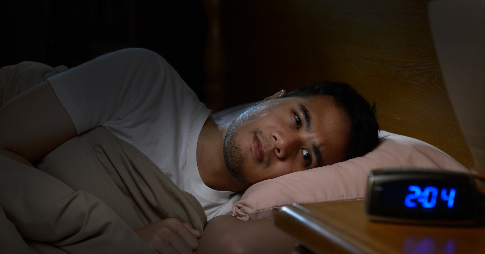 Man awake in bed beside an alarm clock