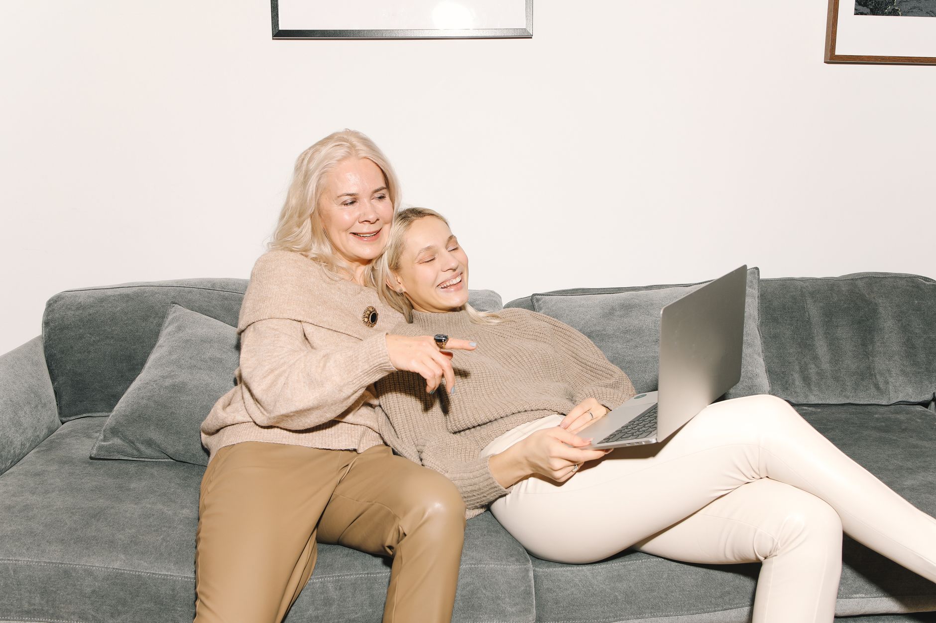 Adult daughter sitting with her mother on a sofa while they use a laptop