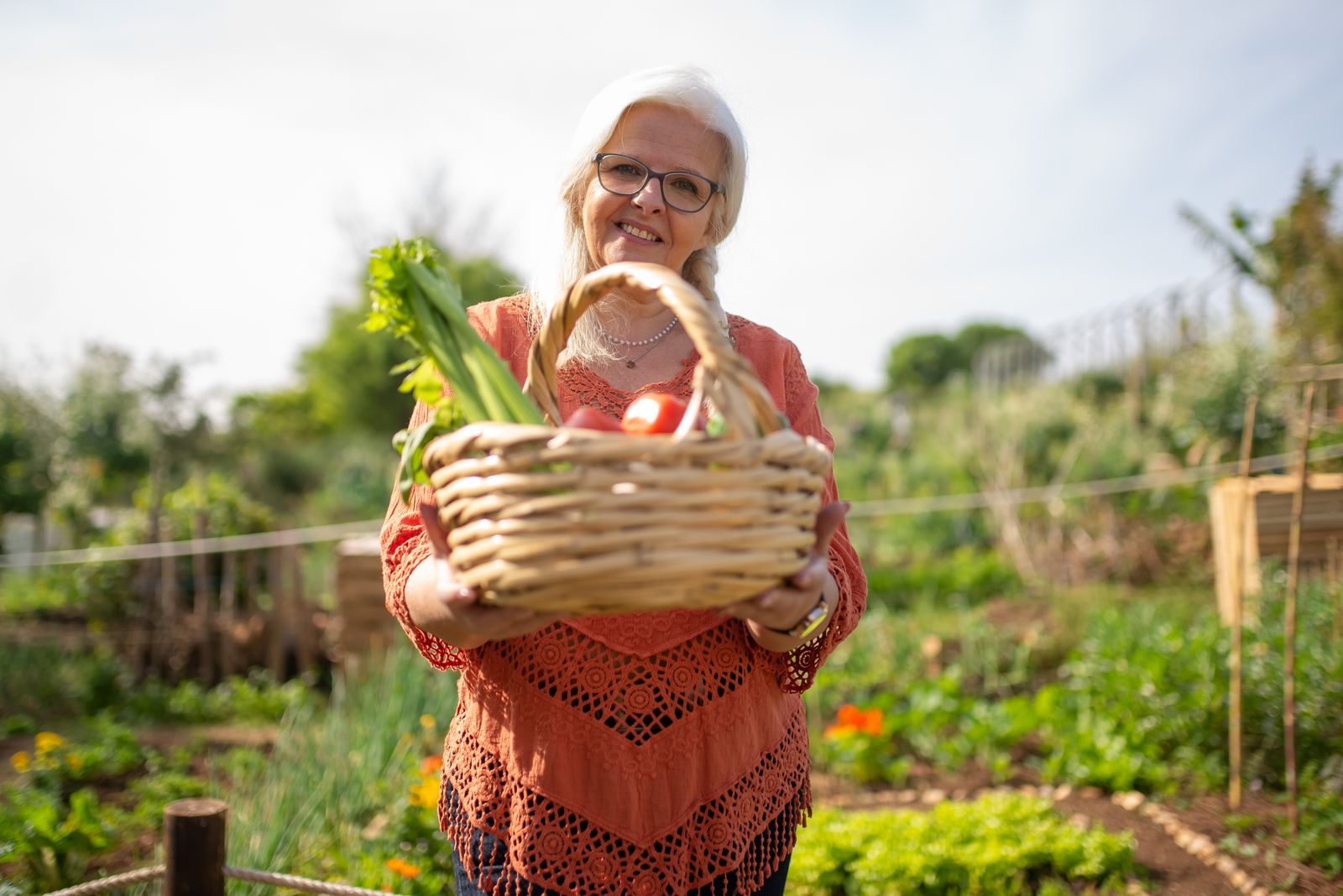 An older woman carrying a basket of vegetables in a community garden