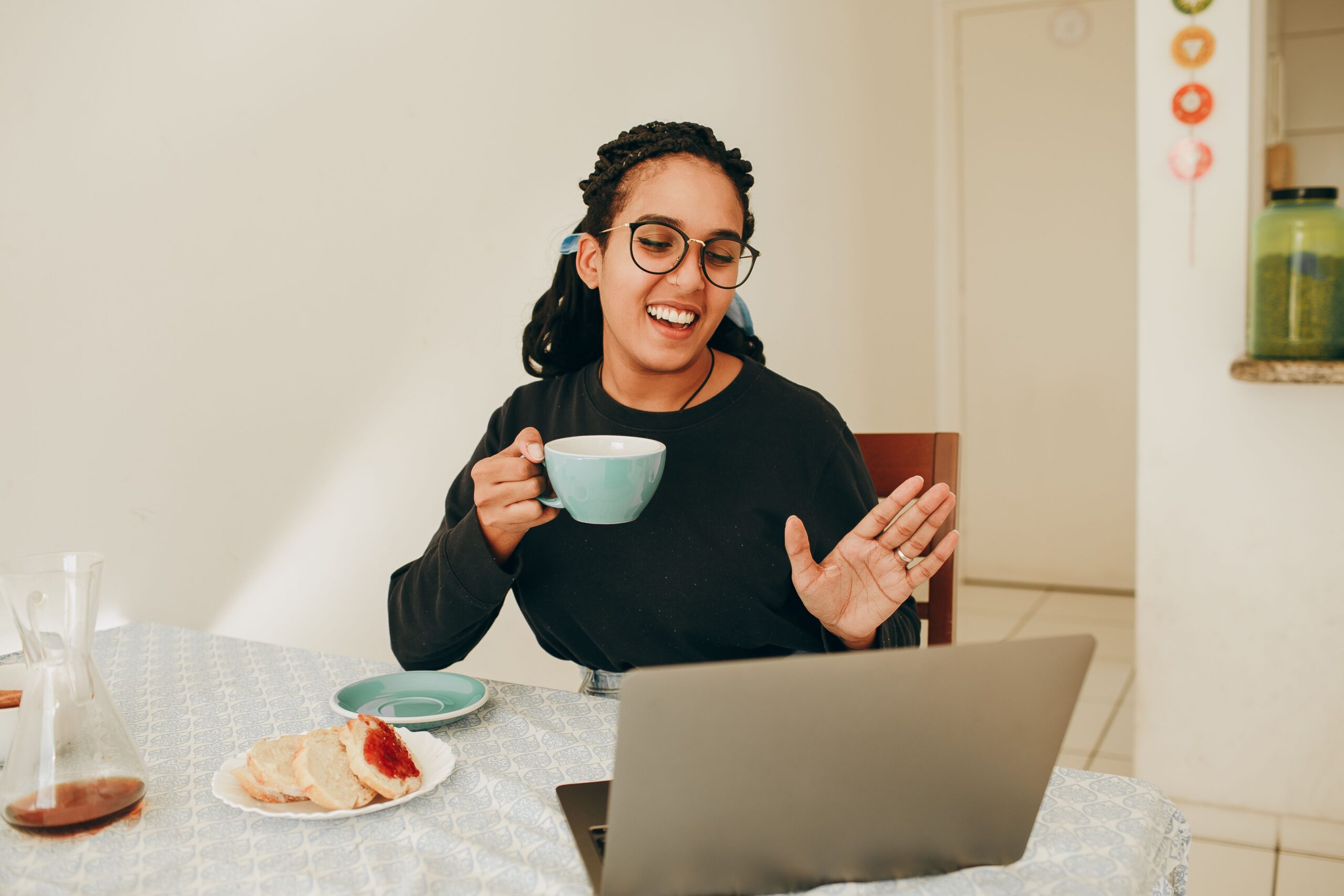 A woman smiling and gesturing while speaking towards a laptop at home