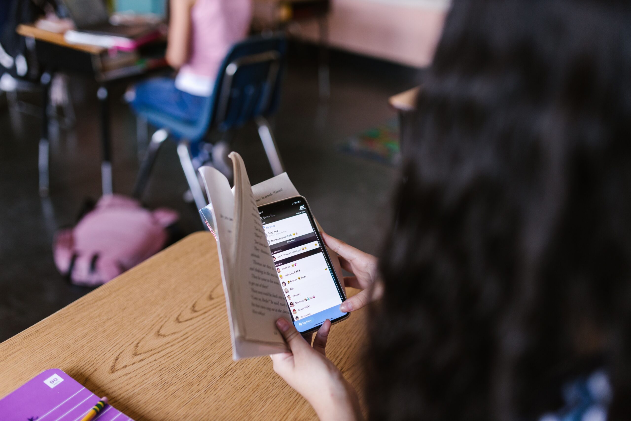 Student looking at a smartphone behind an open book during class
