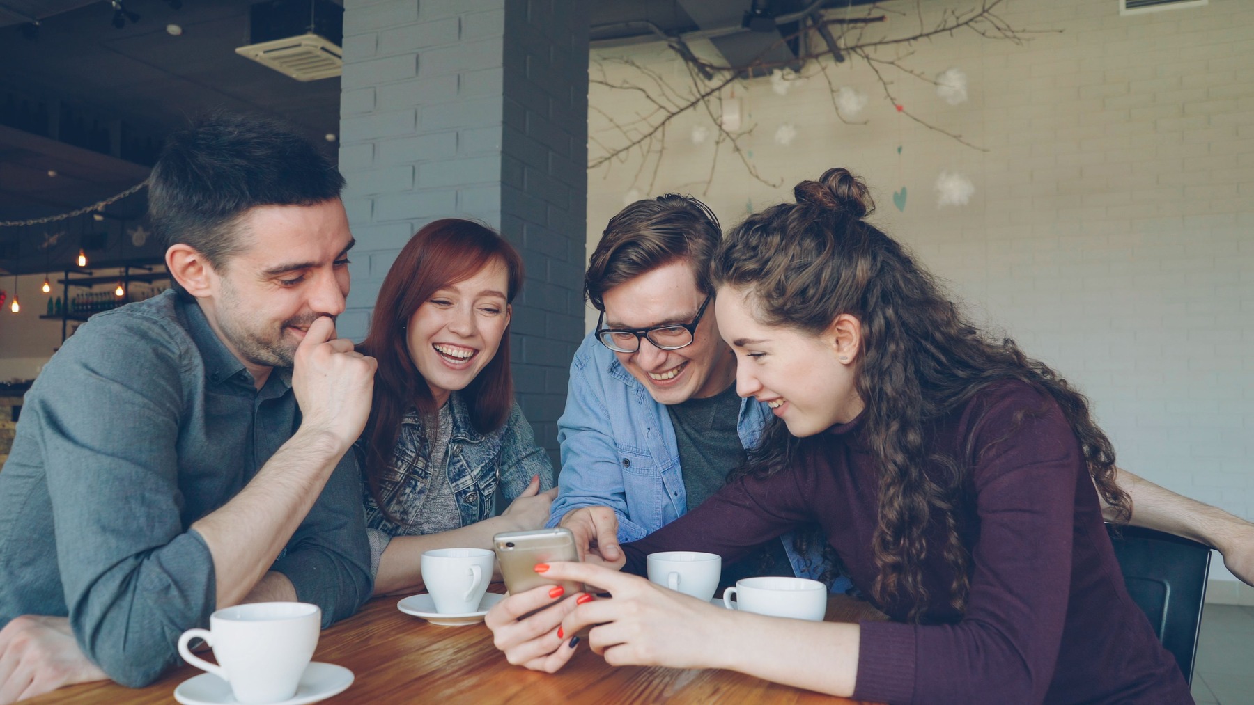 Four friends smiling together over coffee at a cafe table