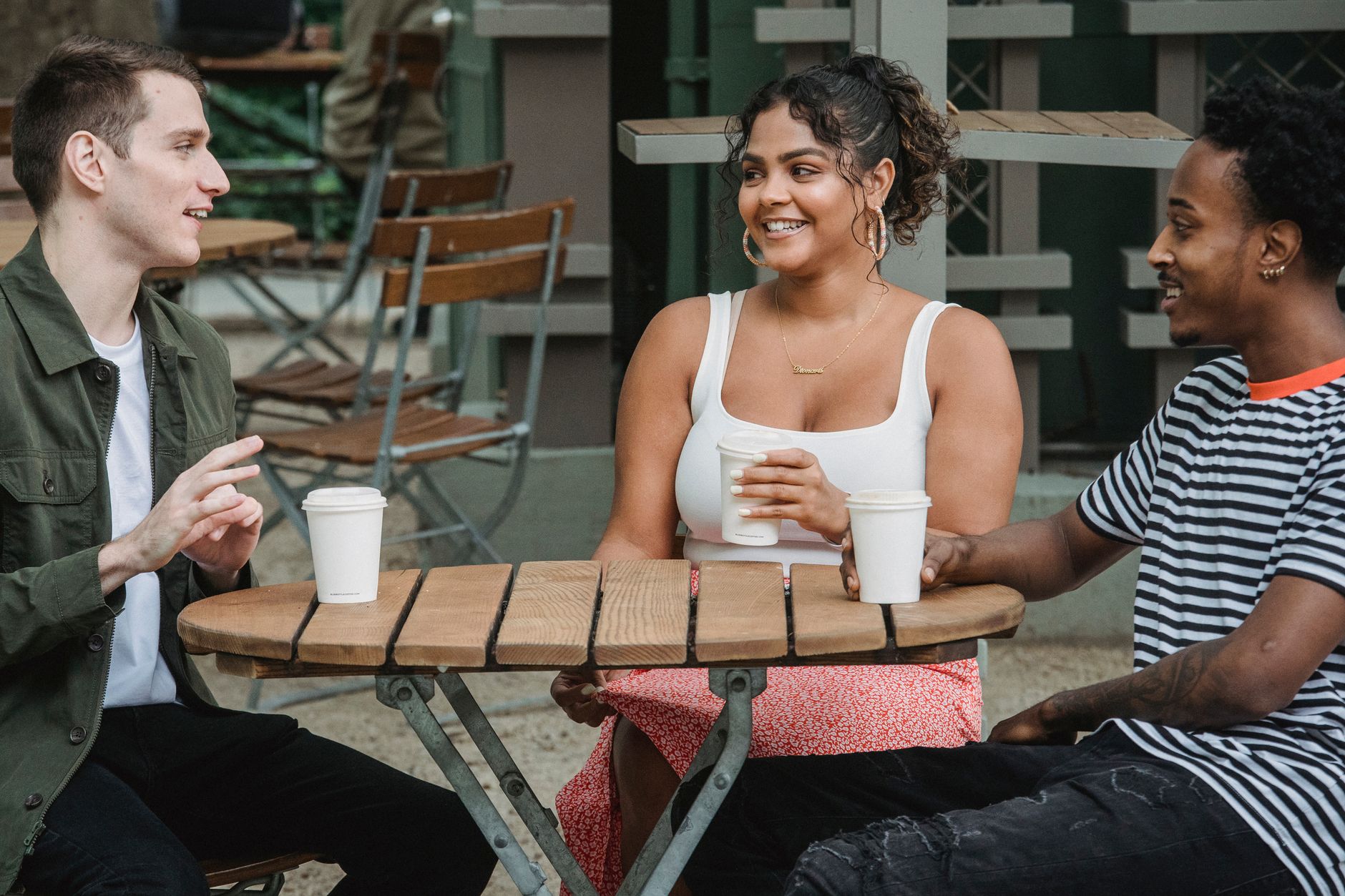 Three friends smiling and talking over coffee at an outdoor cafe