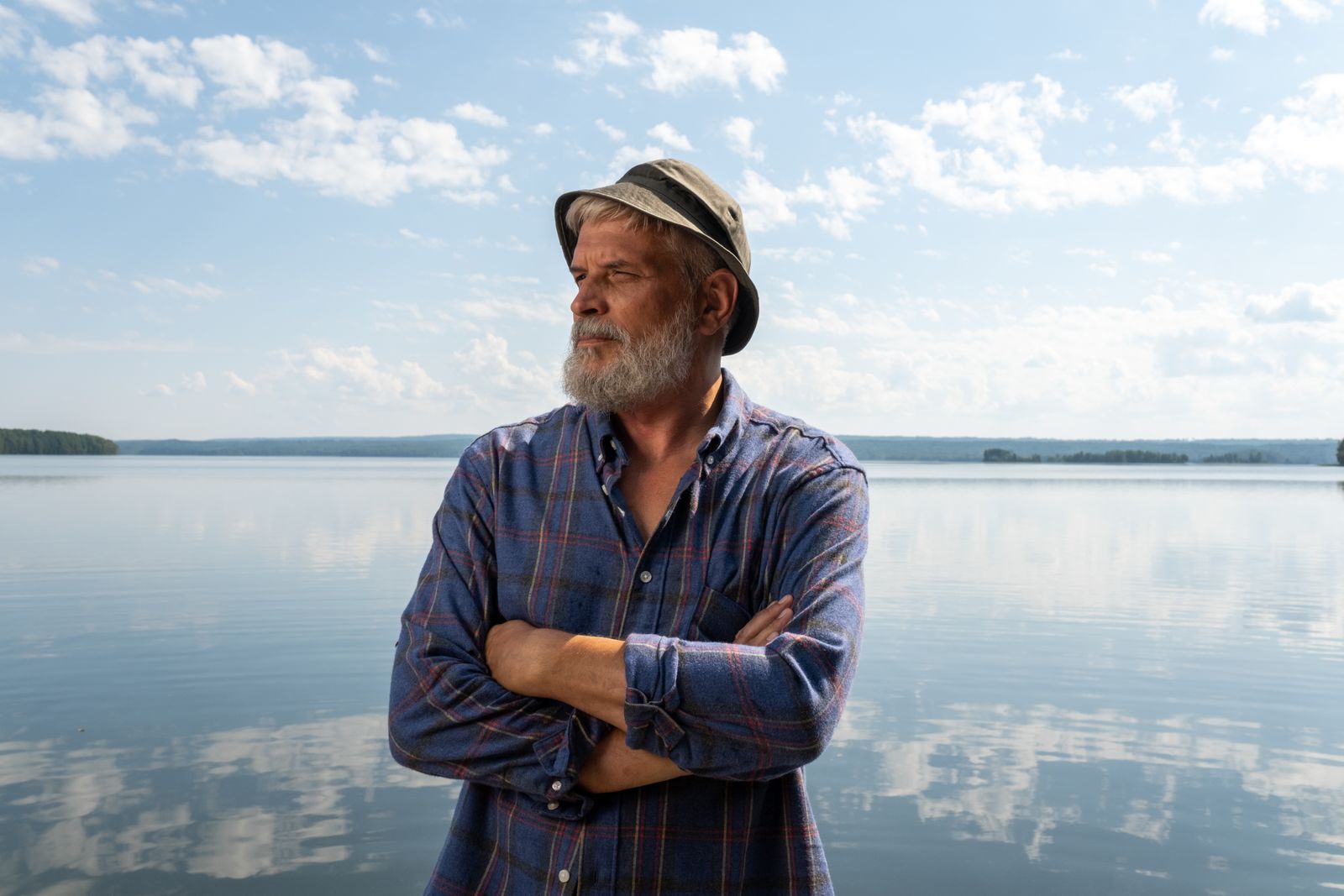A thoughtful older man standing beside a calm lake