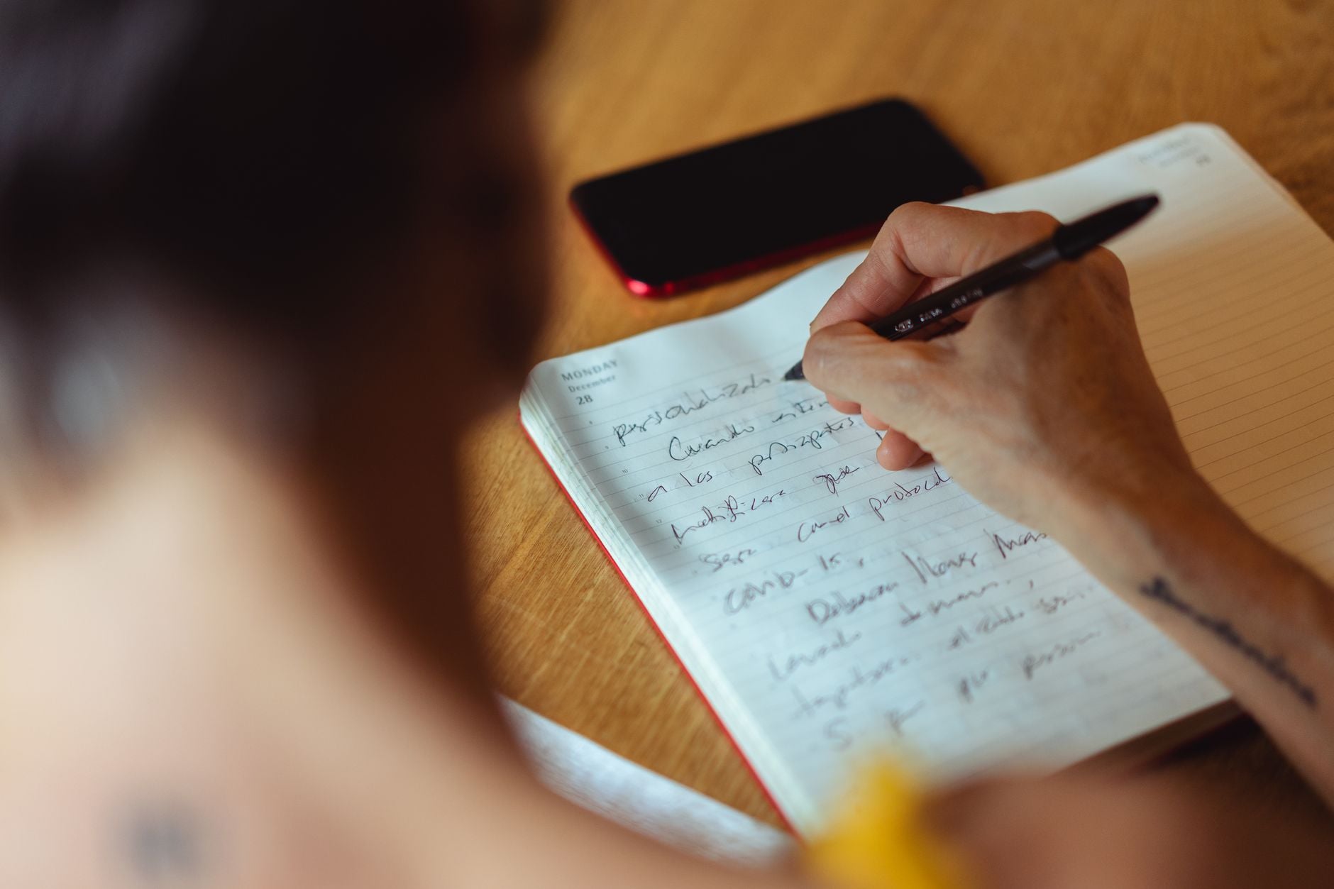 Person beginning a written task in a notebook at a wooden desk