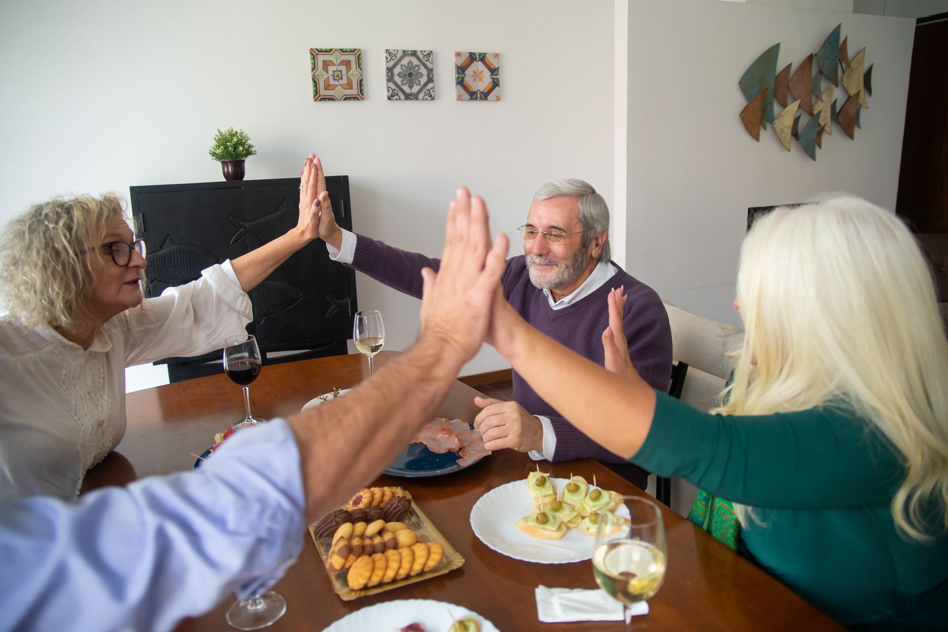 A mixed group of older friends sharing dinner and high-fiving around a table