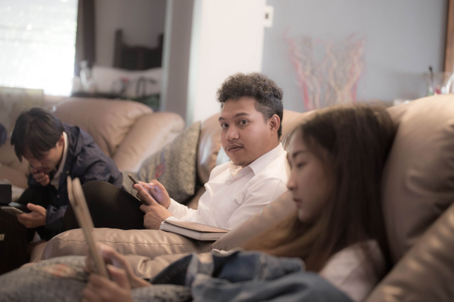Three young adults sitting together indoors while using smartphones