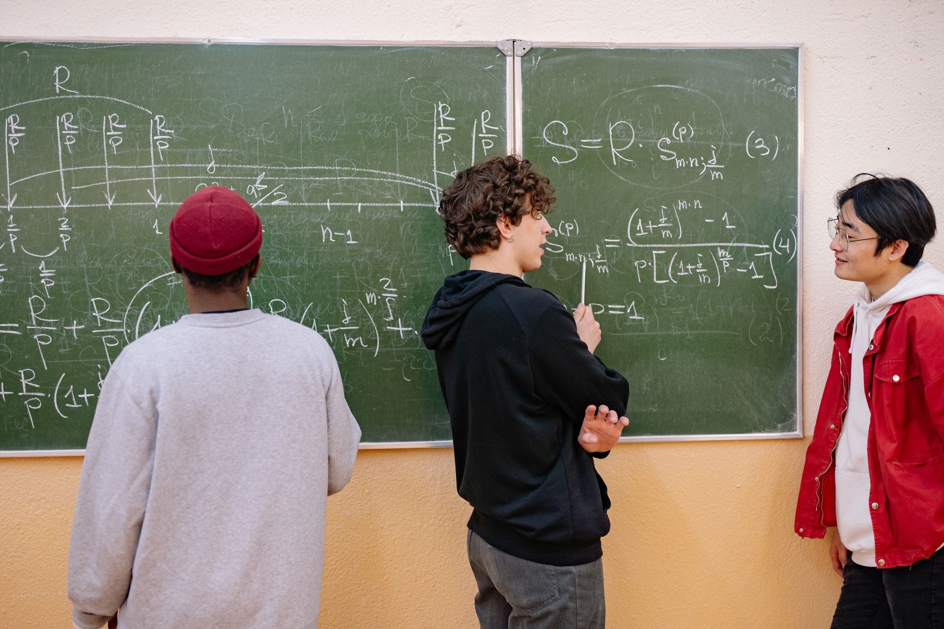 Three students discussing mathematical equations on a classroom blackboard