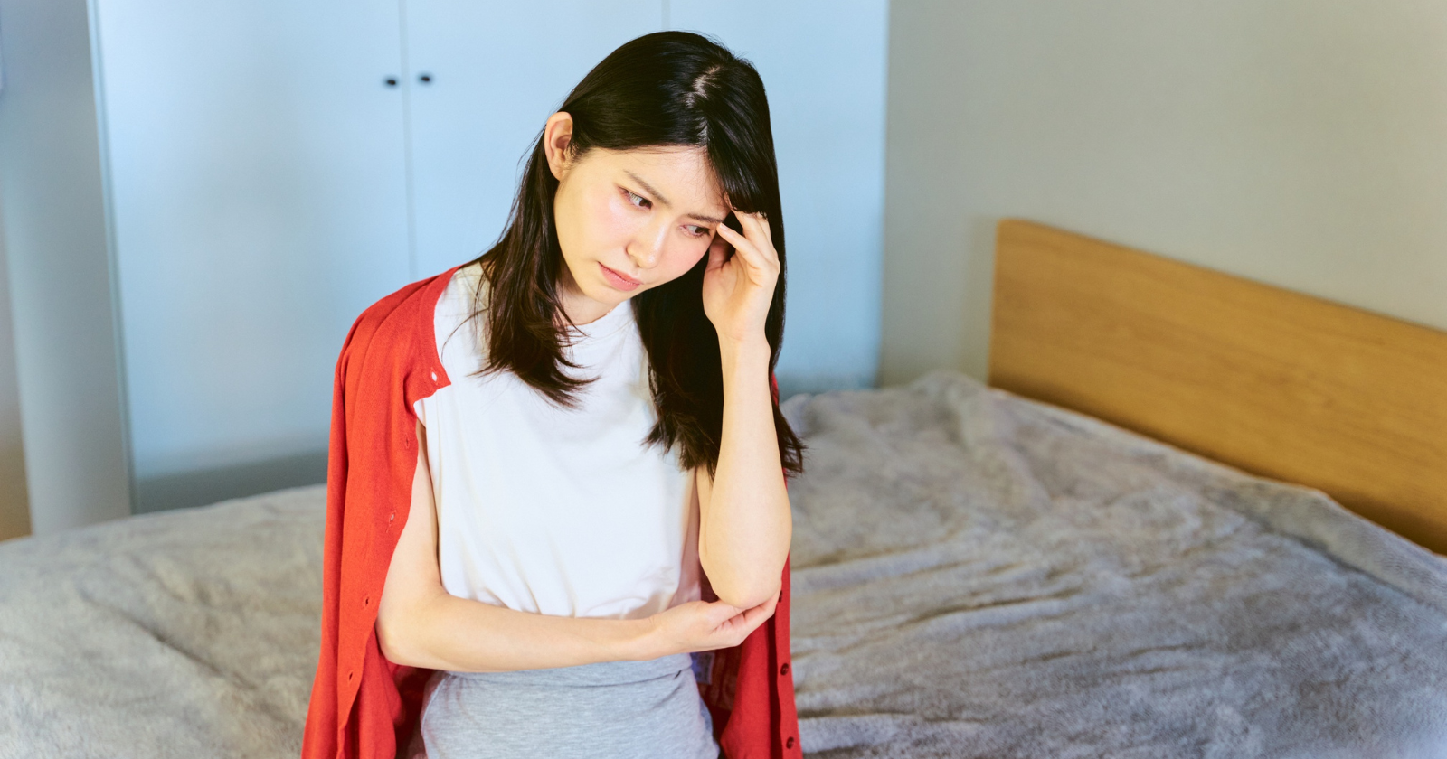 Worried woman sitting on a bed with her hand on her forehead