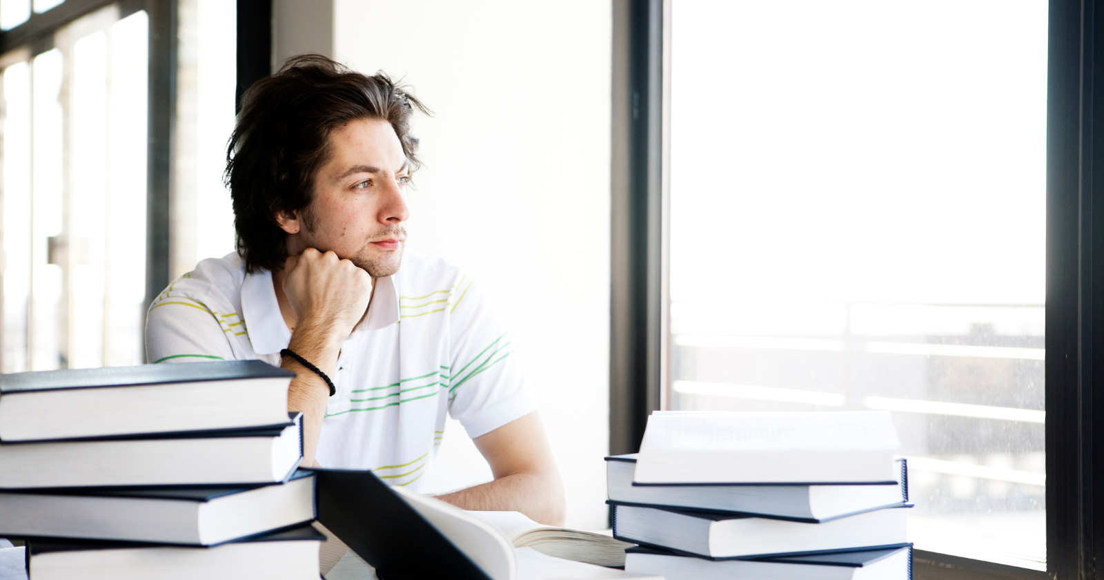 Man sitting among stacks of books and looking out a window