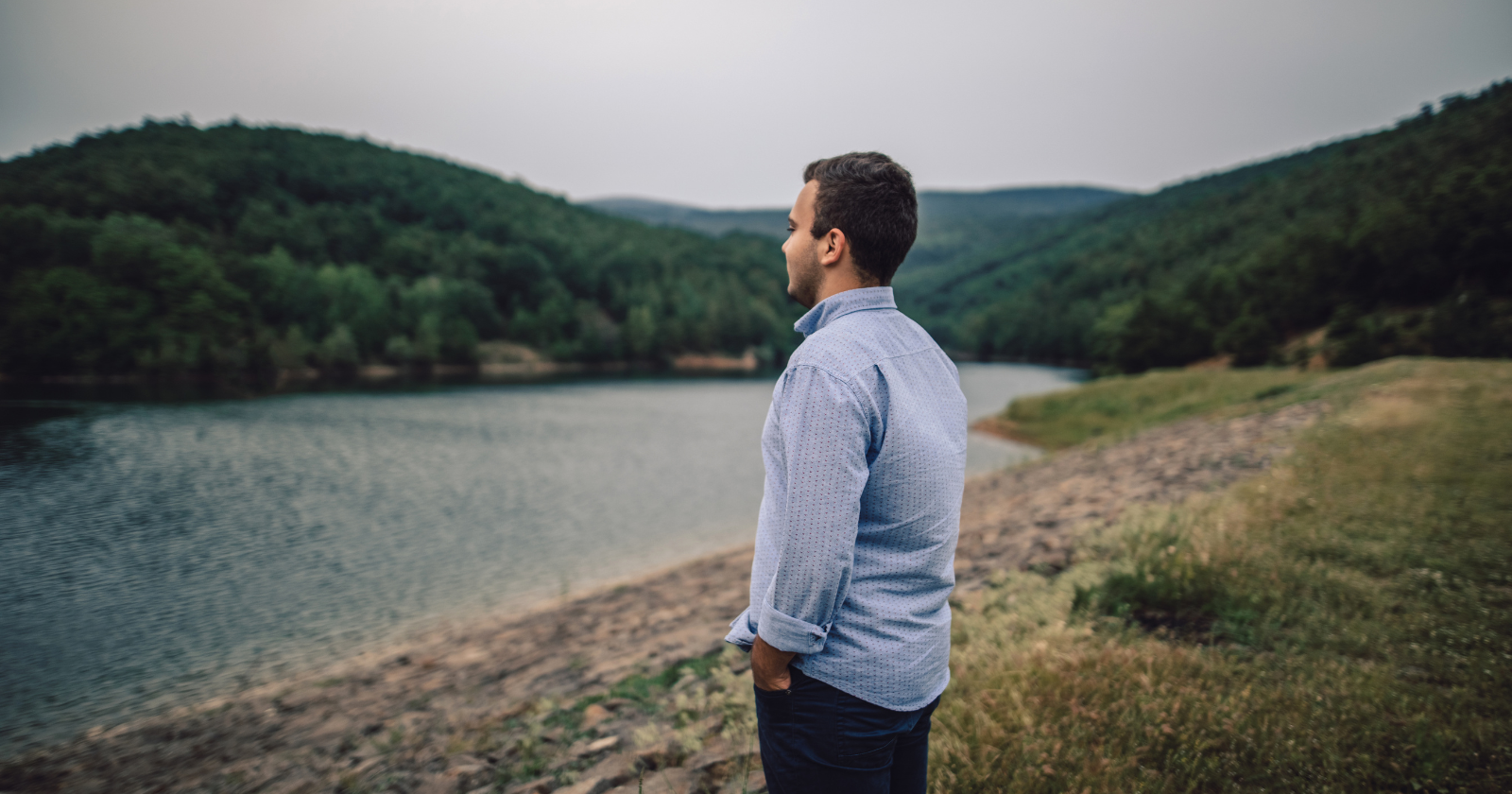 Man standing beside a lake and looking over hills