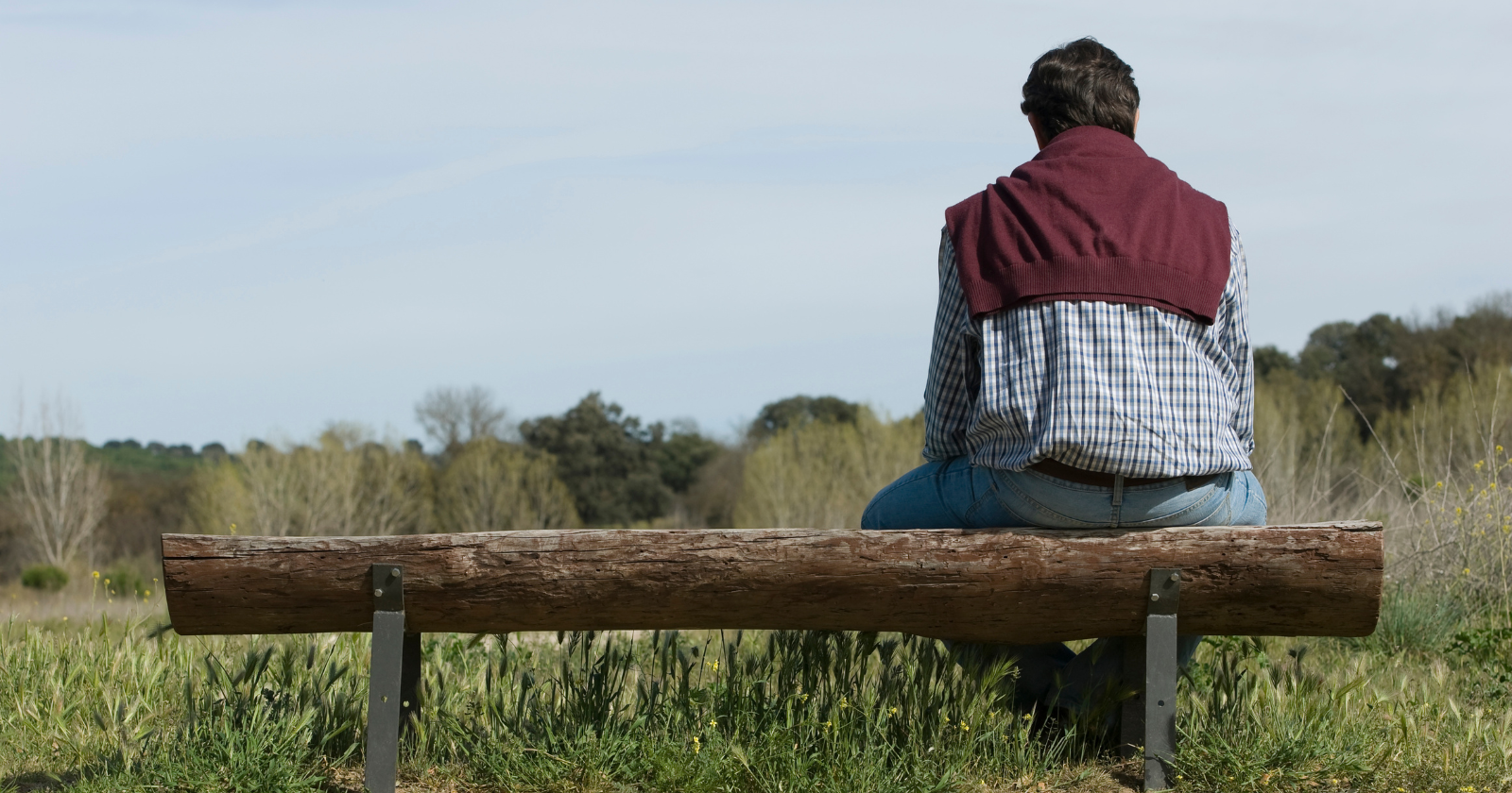 Person sitting alone on a bench overlooking a field