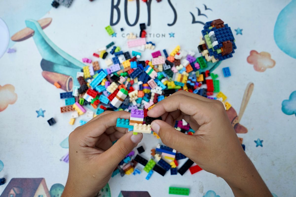 Hands assembling colourful plastic bricks above a pile of building pieces