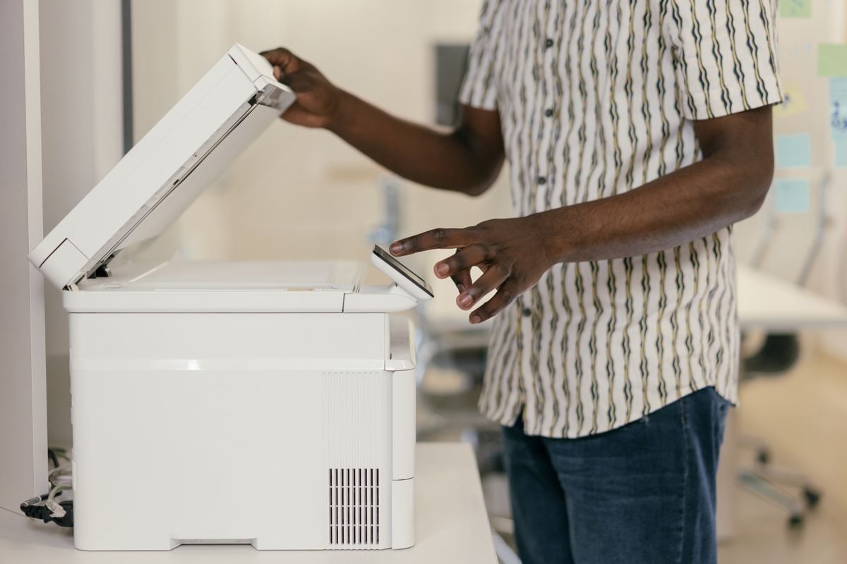 A person lifts the lid of a white photocopier