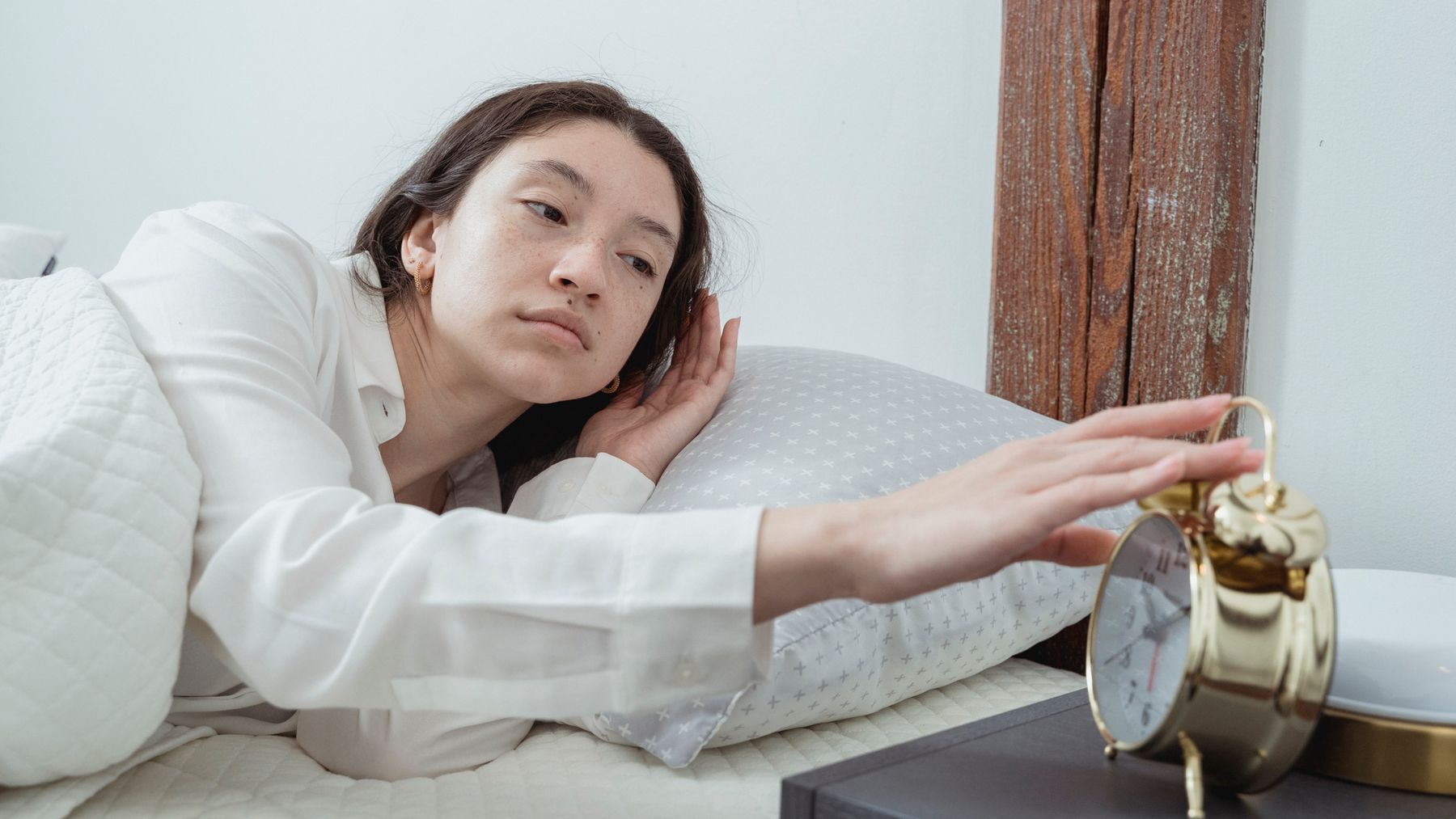 A sleepy woman reaching to switch off an alarm clock in bed