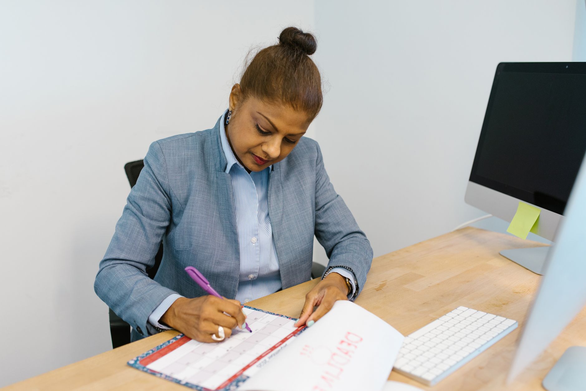 A businesswoman writing in a planner at an office desk