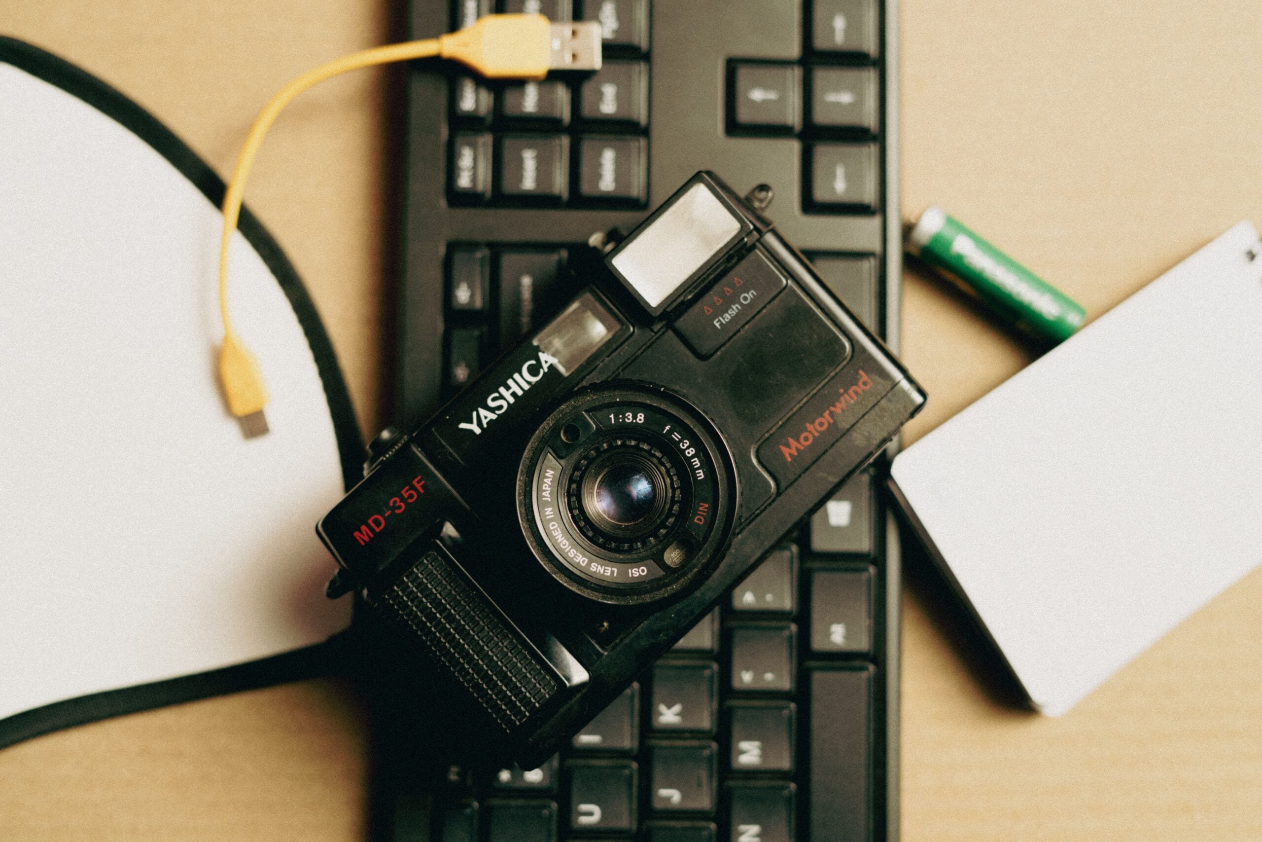 A vintage analogue camera resting on a computer keyboard beside a strip of film