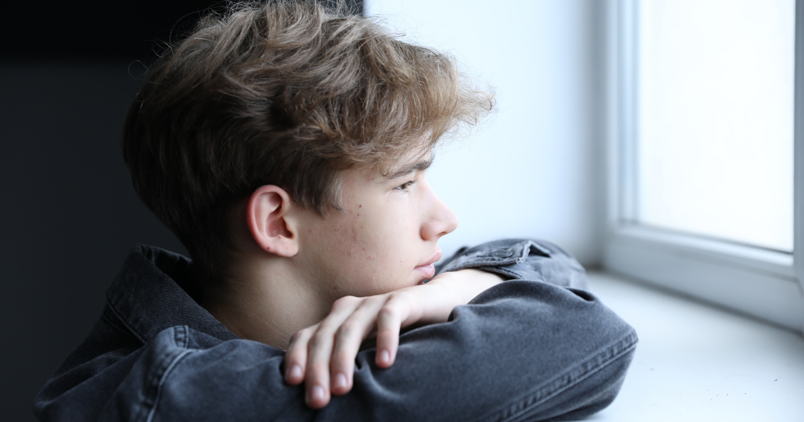 Young man resting his chin on his arms and looking out a window