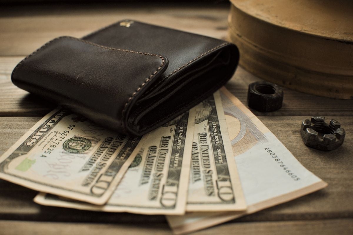 A brown leather wallet with US dollar notes on a table
